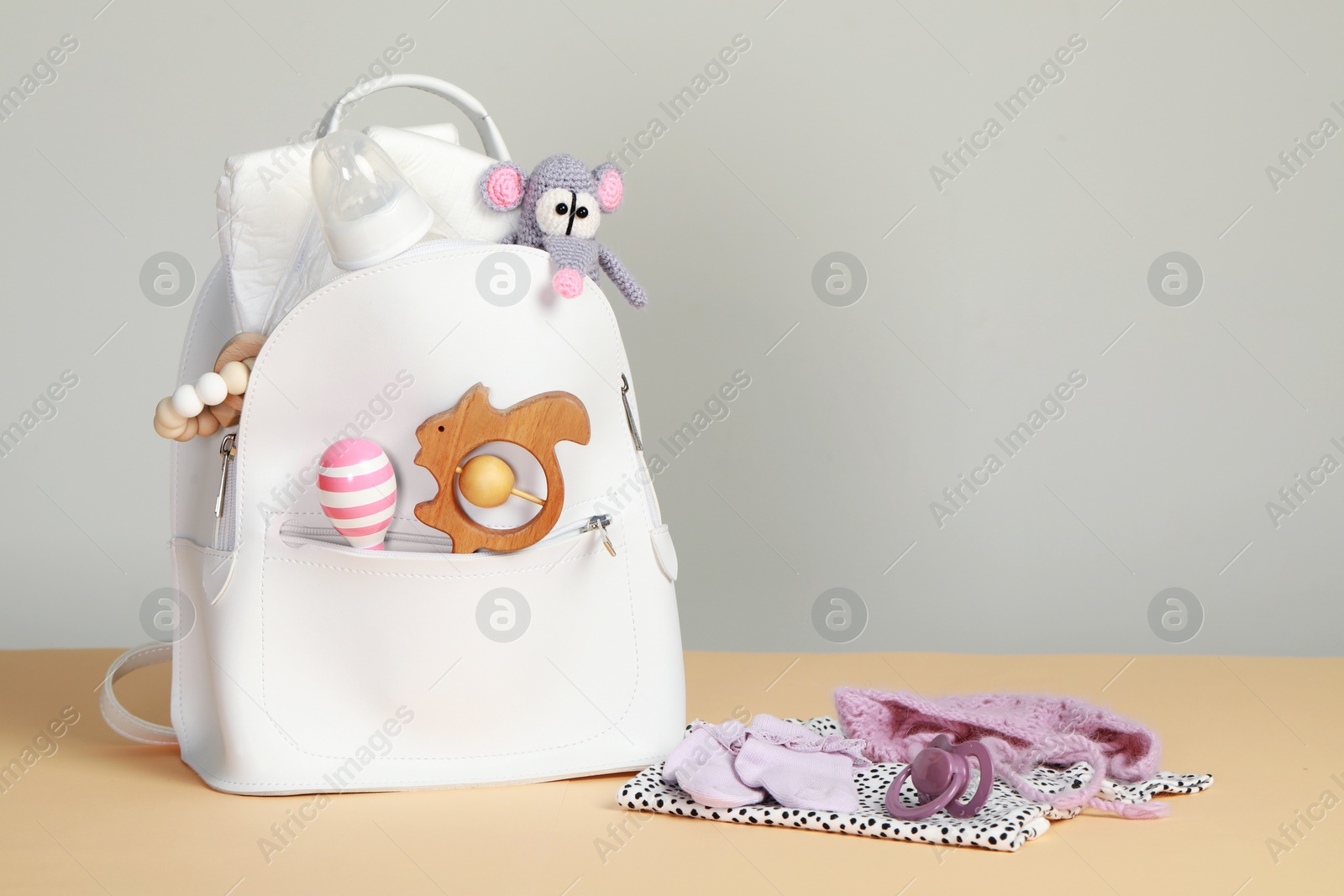 Photo of Mother's backpack with baby's stuff on beige surface against grey background. Space for text