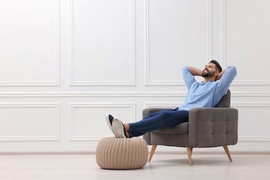 Photo of Handsome man relaxing in armchair near white wall indoors, space for text