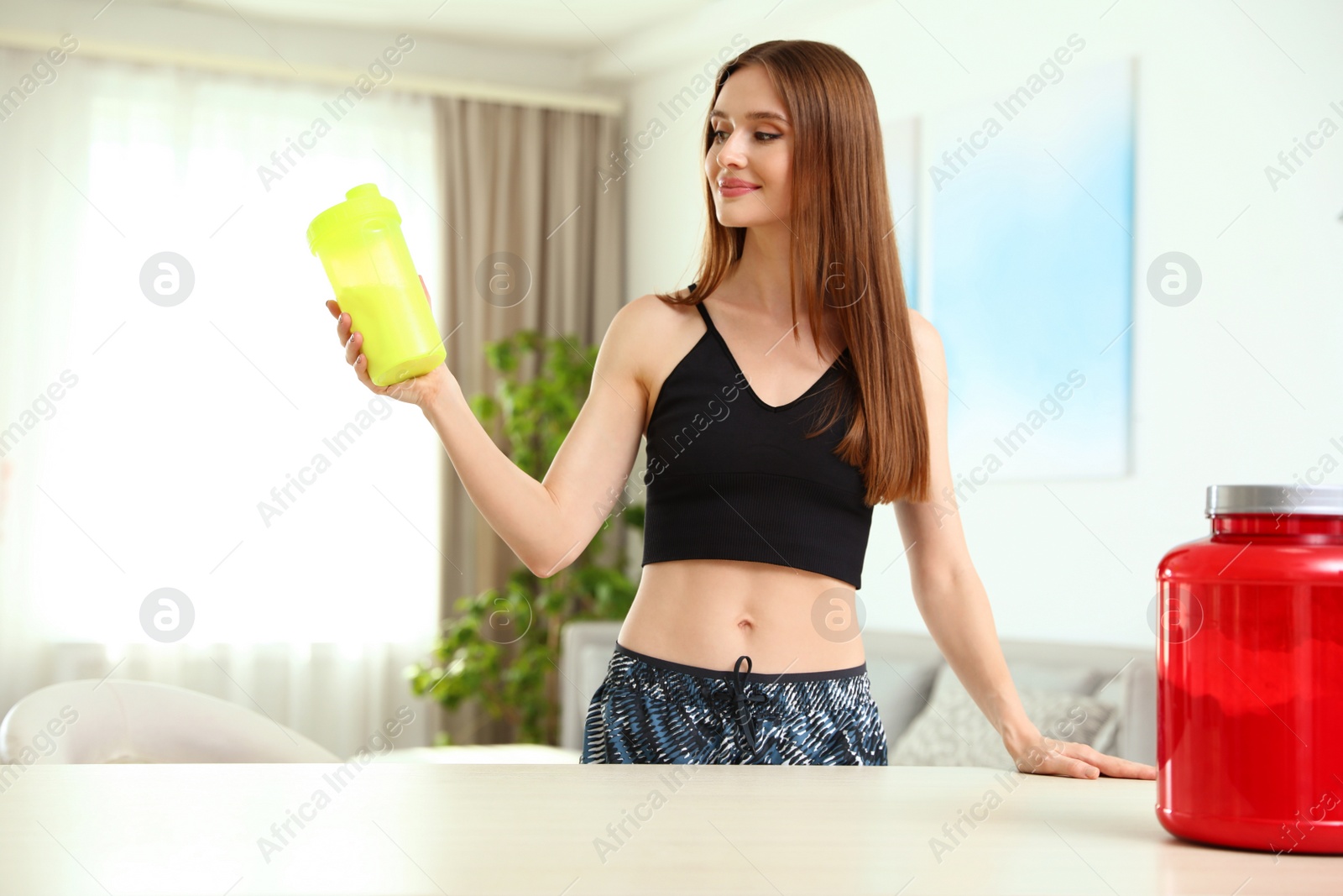 Photo of Young woman with bottle of protein shake at home