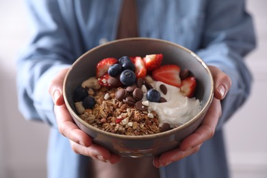 Photo of Woman holding bowl of tasty granola, closeup