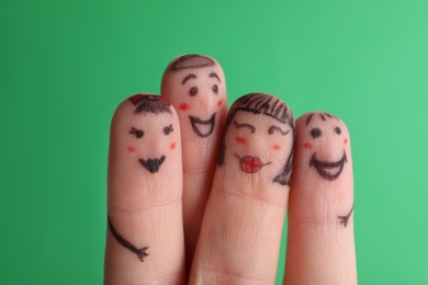 Photo of Four fingers with drawings of happy faces on green background