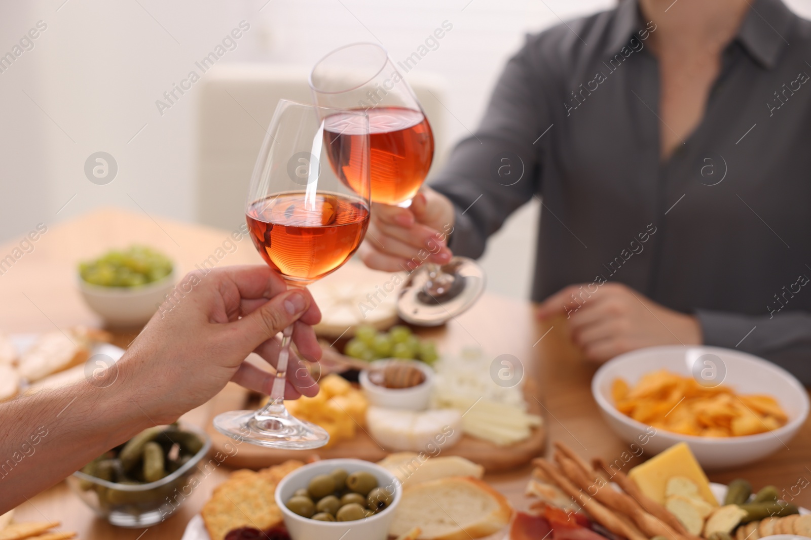 Photo of People clinking glasses with rose wine above table indoors, closeup