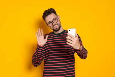 Handsome man in striped sweatshirt and eyeglasses with phone on yellow background