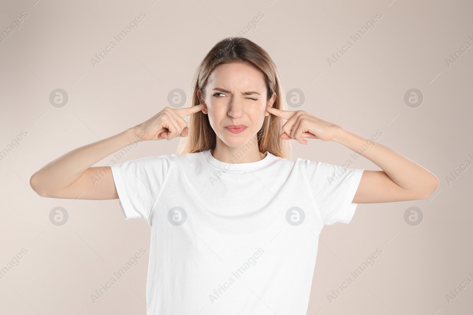 Photo of Emotional young woman covering her ears with fingers on beige background