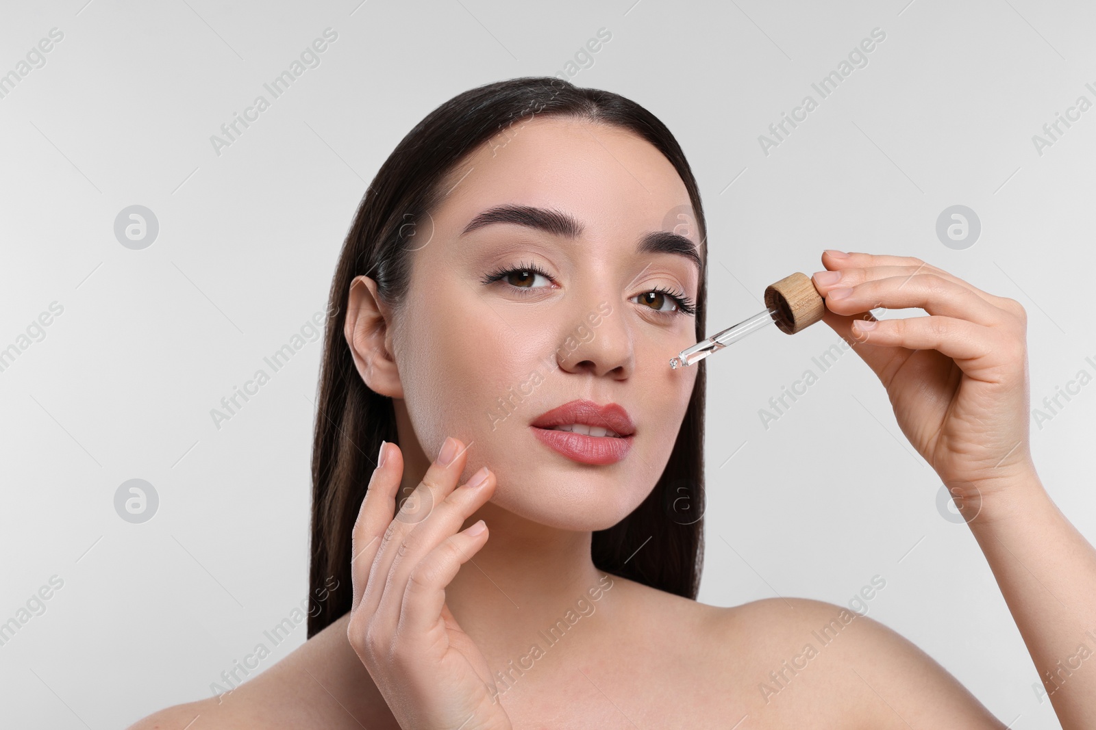 Photo of Young woman applying essential oil onto face on white background, closeup