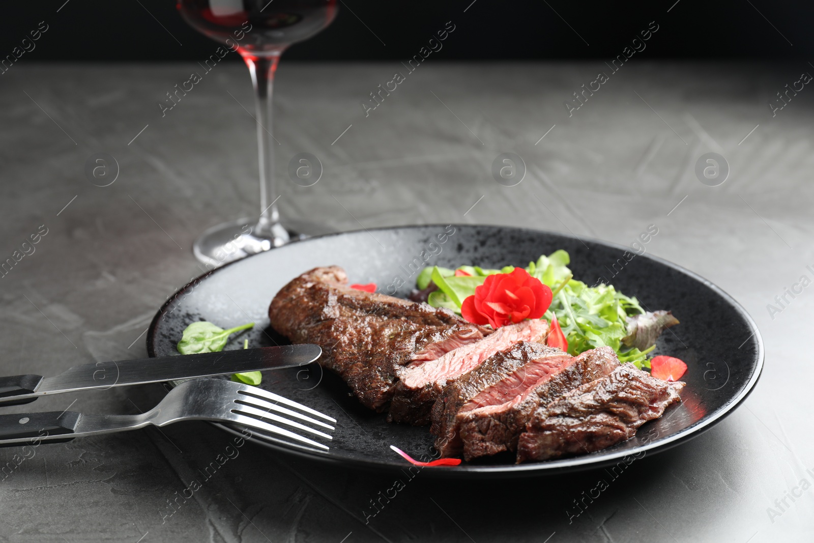 Photo of Delicious grilled beef meat served with greens on grey table