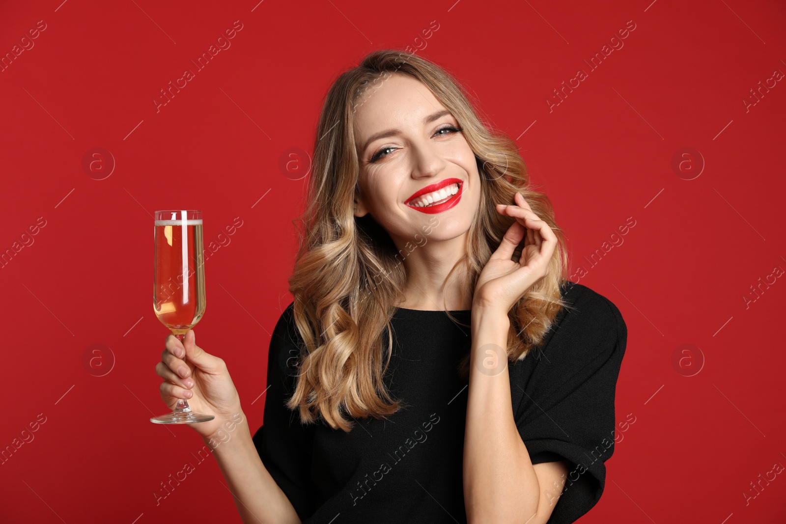 Photo of Happy young woman with glass of champagne on red background. Christmas celebration