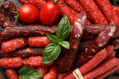 Different thin dry smoked sausages, basil and tomatoes on table, flat lay