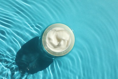 Photo of Jar with moisturizing cream in water on light blue background, top view