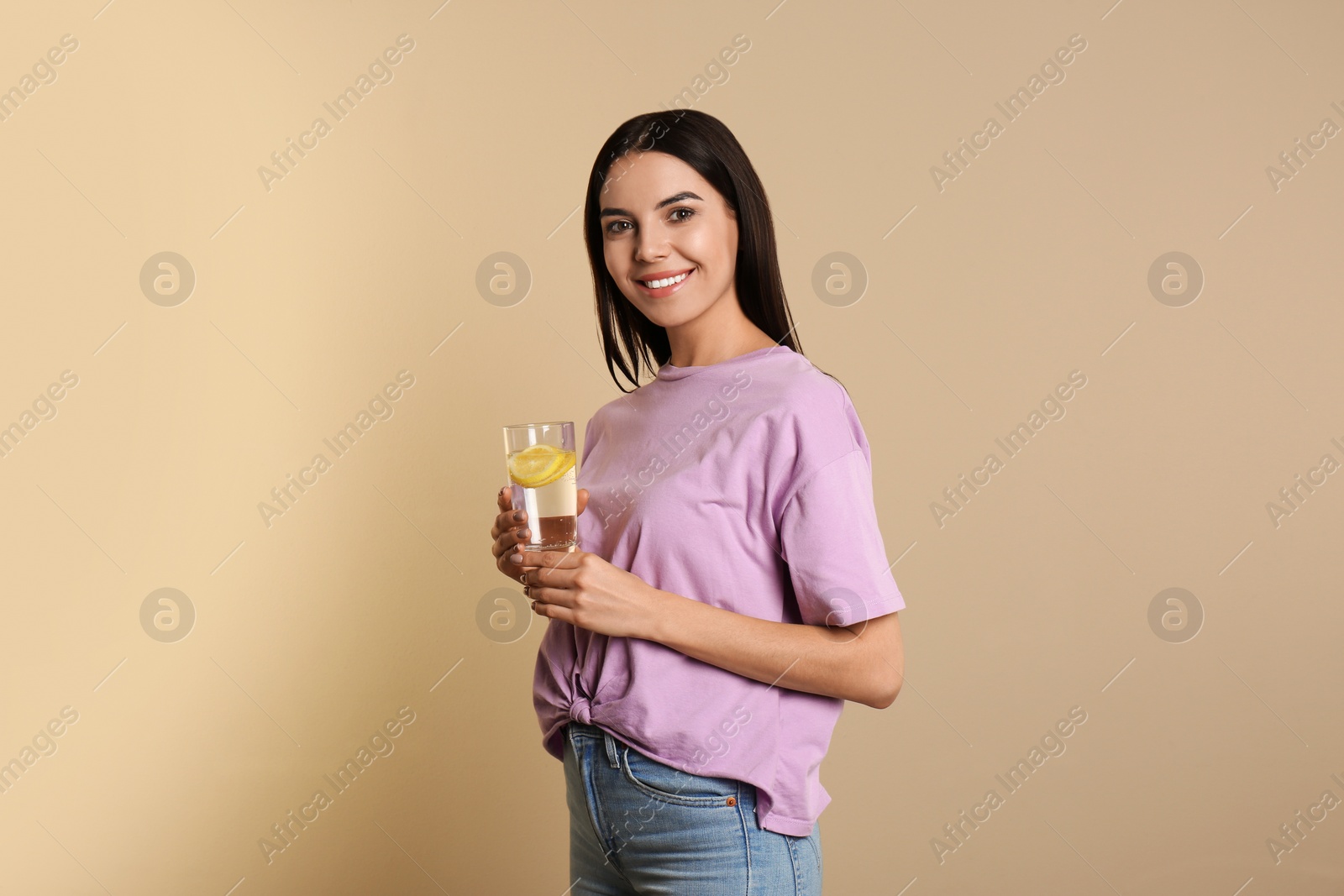 Photo of Beautiful young woman with tasty lemon water on beige background
