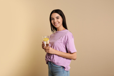 Beautiful young woman with tasty lemon water on beige background