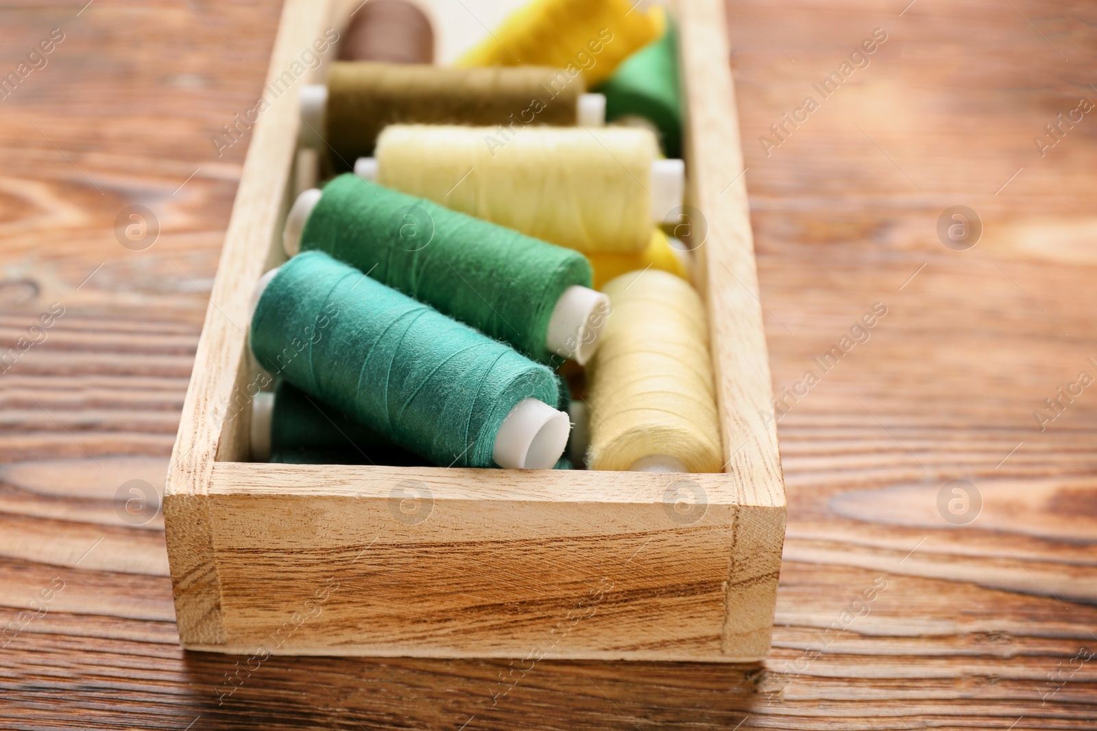 Photo of Container with set of color sewing threads on wooden background