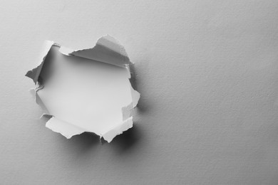 Hole in white paper on light background, space for text