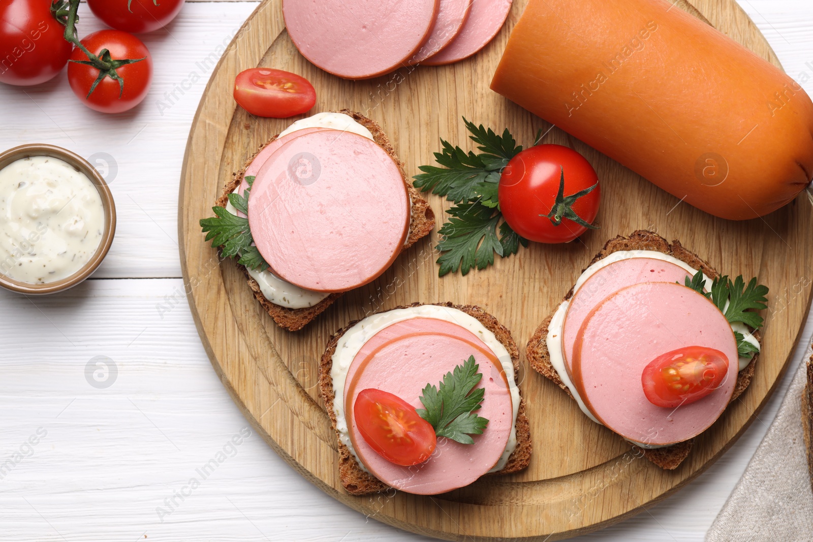 Photo of Delicious sandwiches with boiled sausage, tomato and sauce on white wooden table, flat lay