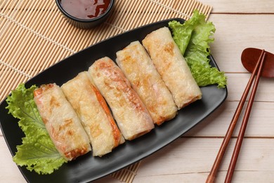 Photo of Delicious fried spring rolls, sauce and chopsticks on light wooden table, flat lay