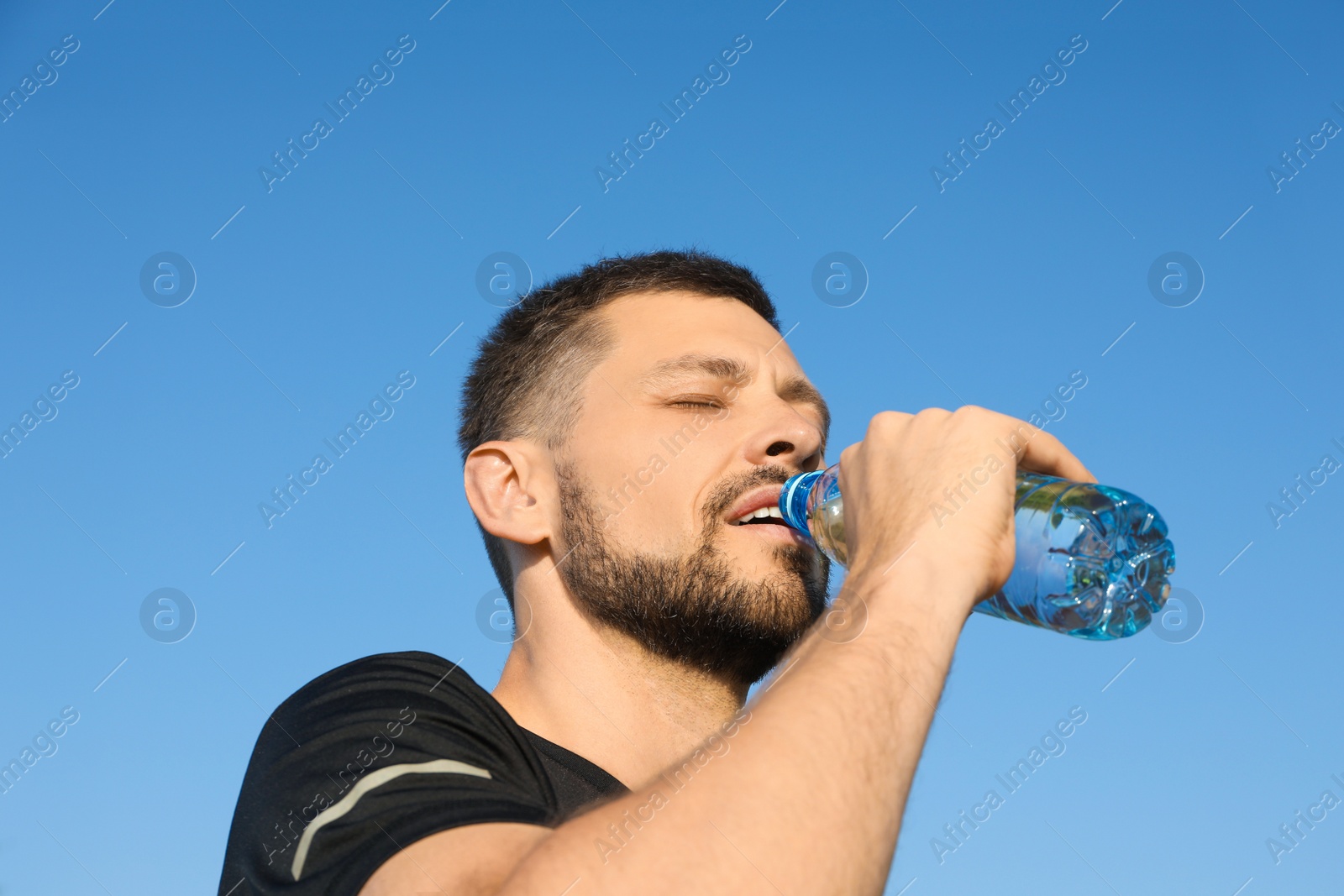 Photo of Man drinking water against blue sky on hot summer day. Refreshing drink
