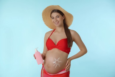 Photo of Young pregnant woman with sun protection cream on light blue background