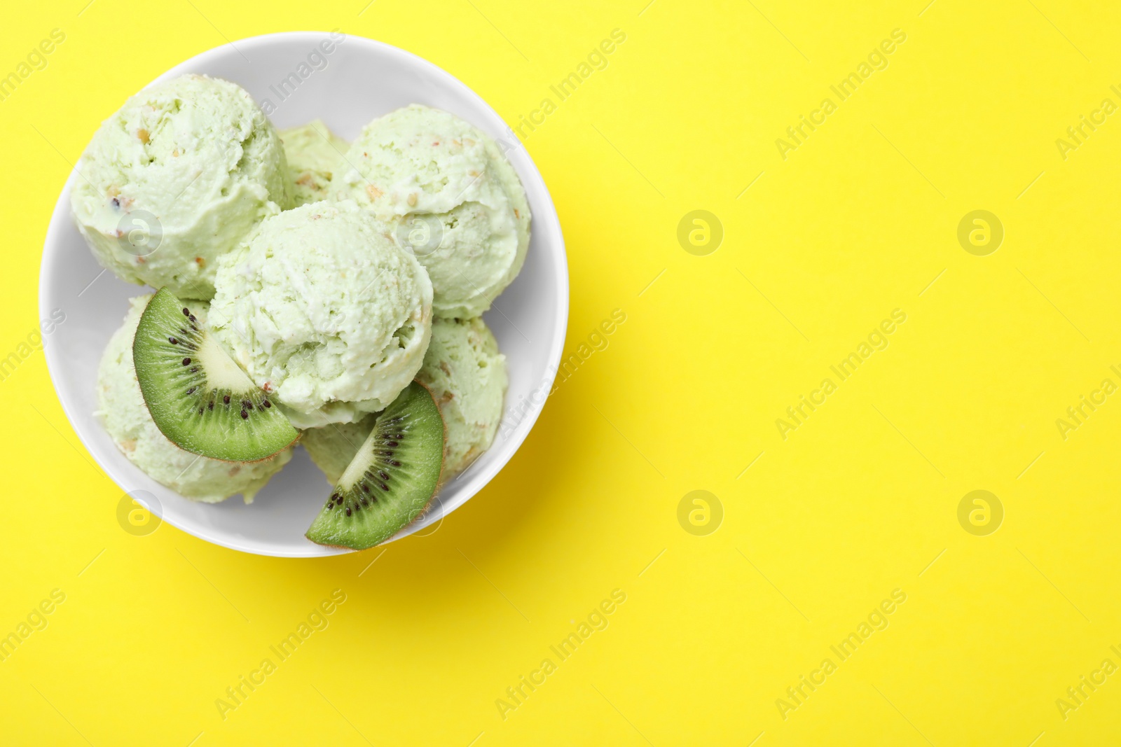 Photo of Delicious kiwi ice cream on yellow background, top view. Space for text