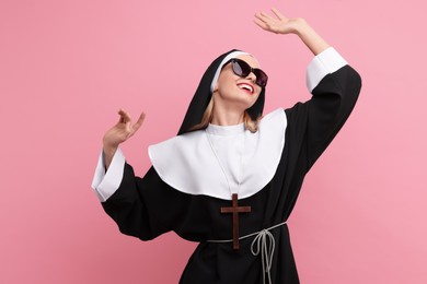 Photo of Happy woman in nun habit and sunglasses against pink background
