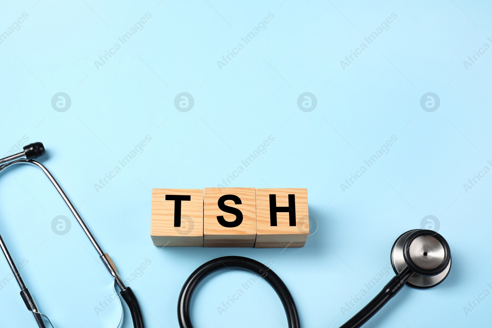 Photo of Endocrinology. Stethoscope and wooden cubes with thyroid hormones on light blue background. Space for text