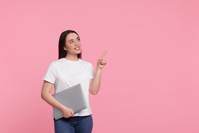 Smiling young woman with laptop on pink background, space for text