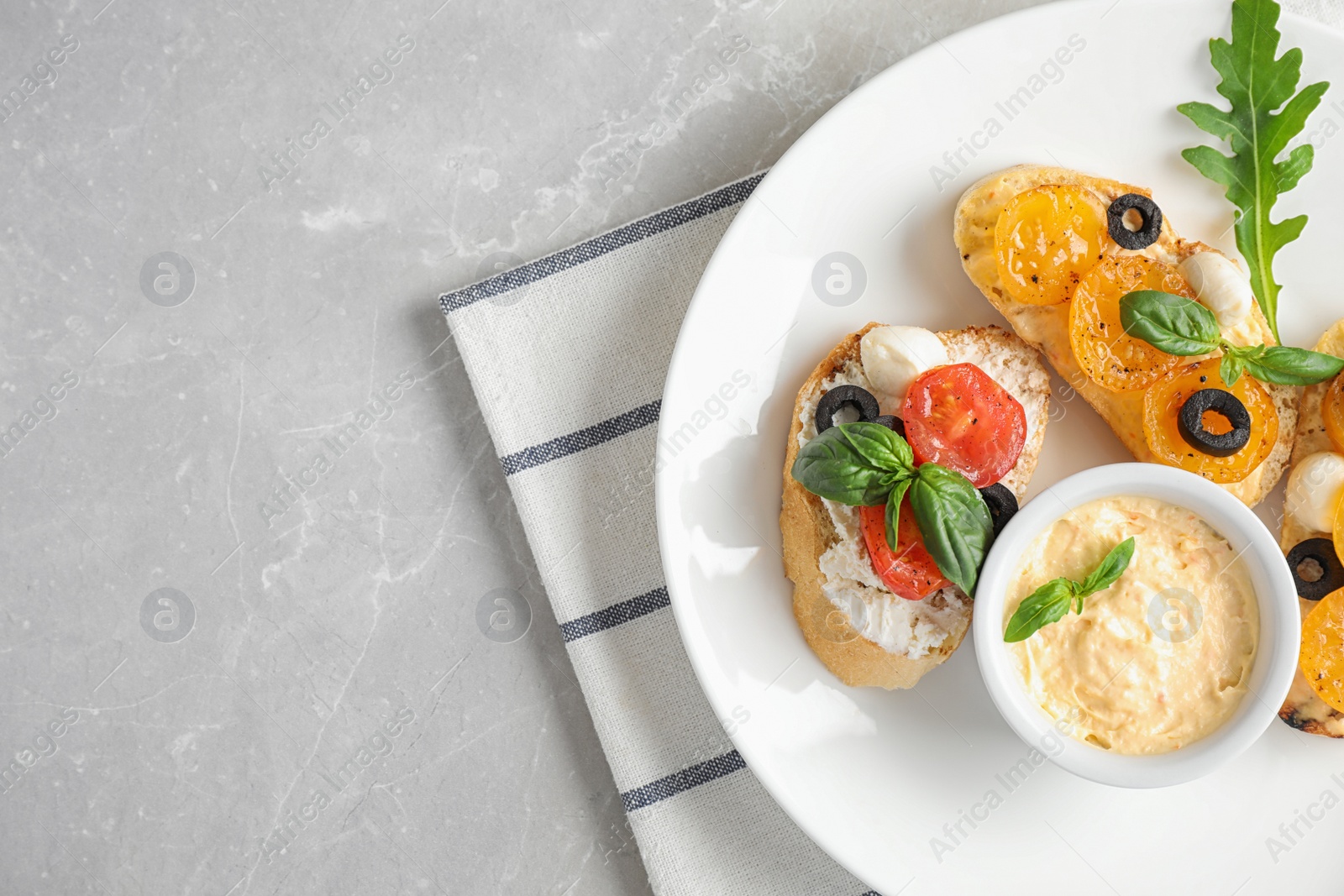 Photo of Plate of delicious tomato bruschettas on light grey marble background, top view. Space for text