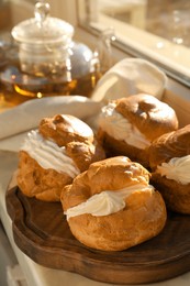 Photo of Delicious profiteroles filled with cream on window sill indoors, closeup