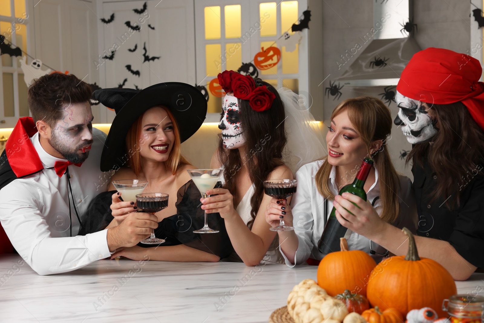 Photo of Group of people in scary costumes with cocktails celebrating Halloween indoors