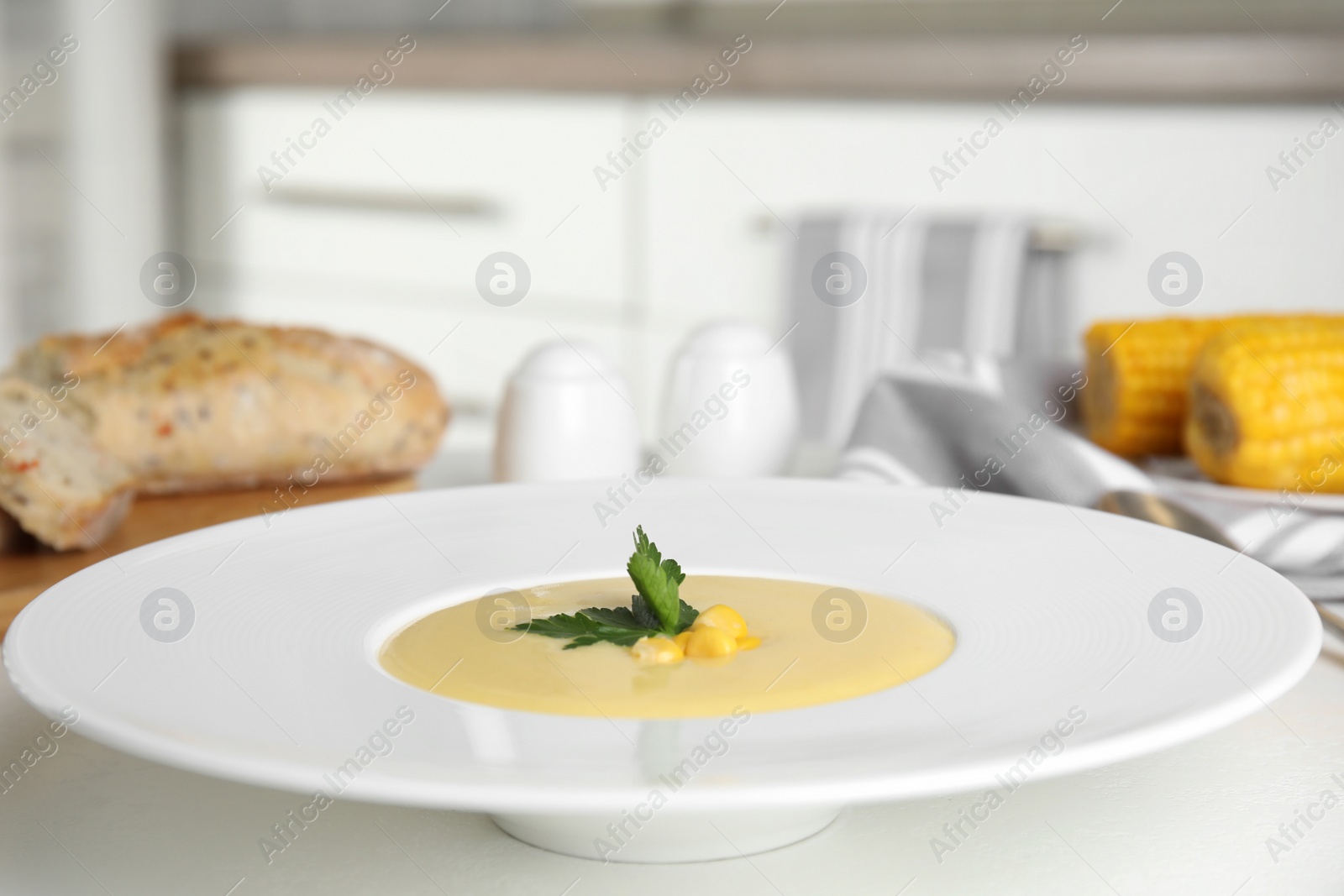 Photo of Delicious corn cream soup served on white table indoors