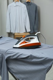 Photo of Modern iron and grey shirt near rack with clean clothes indoors