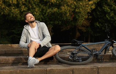 Photo of Man with injured knee on steps near bicycle outdoors