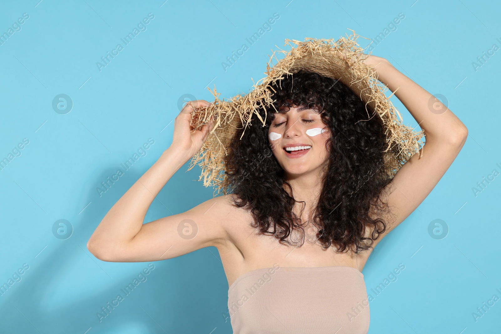 Photo of Beautiful young woman in straw hat with sun protection cream on her face against light blue background