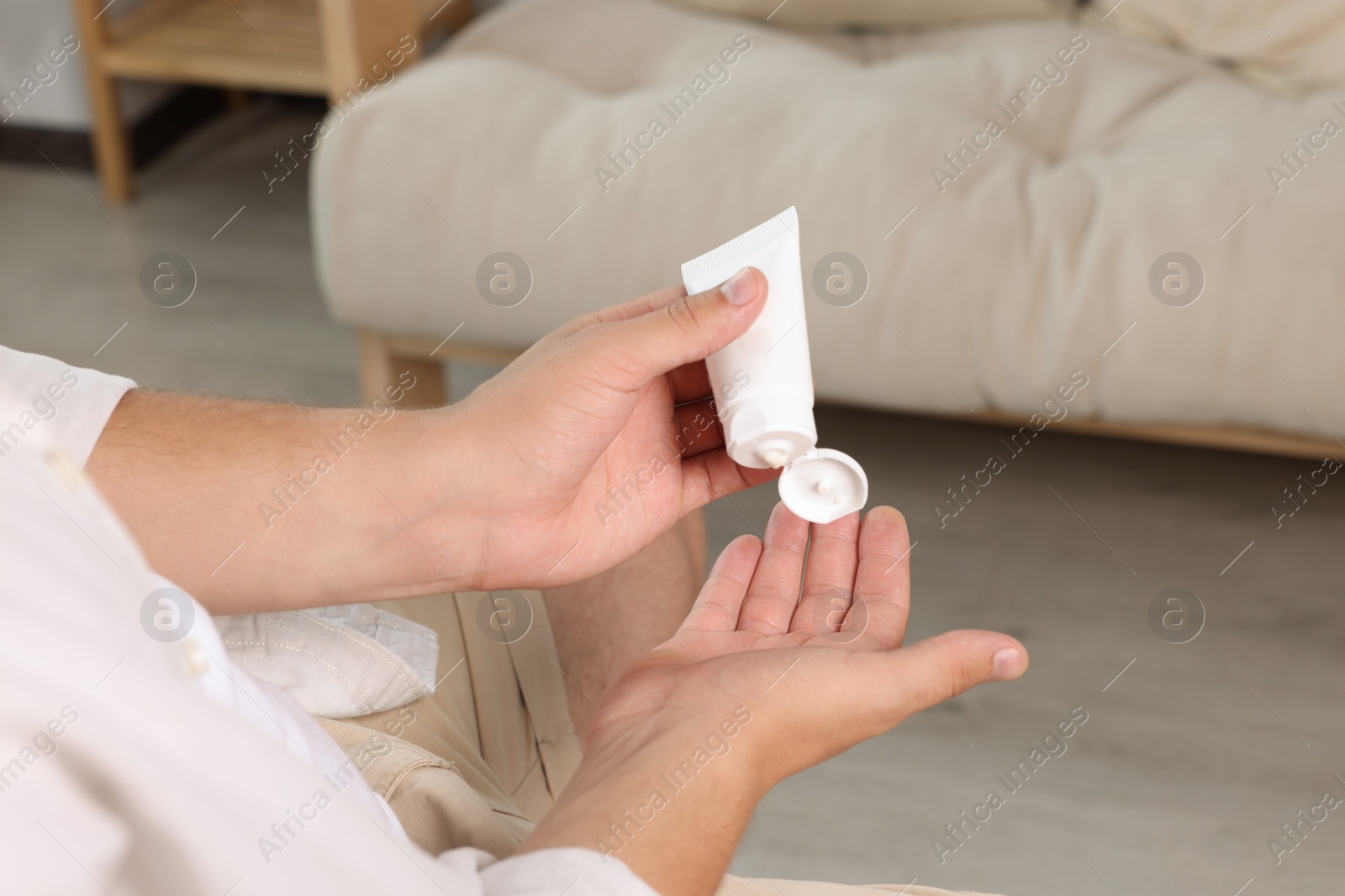 Photo of Man applying hand cream from tube at home, closeup