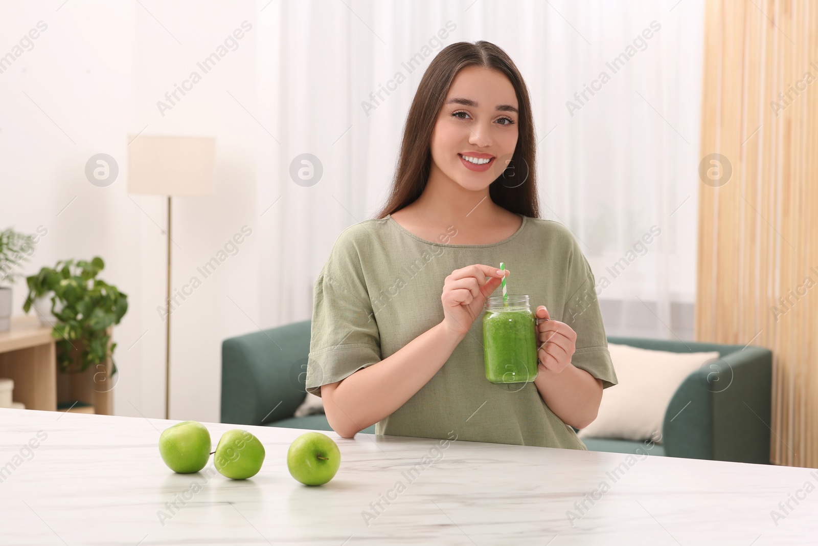 Photo of Beautiful young woman with mason jar of delicious smoothie and apples at home