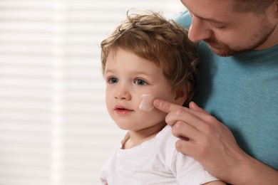 Photo of Father applying ointment onto his son`s cheek indoors. Space for text