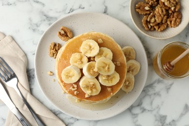 Photo of Delicious pancakes with bananas, walnuts and honey served on white marble table, flat lay