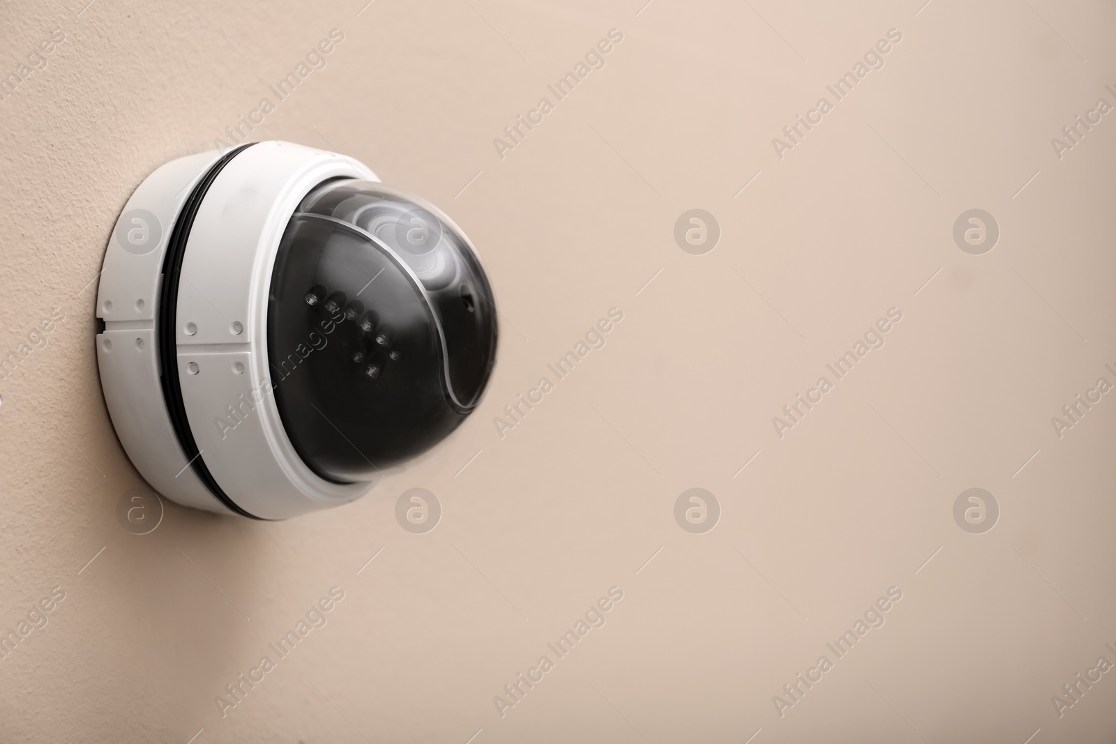 Photo of Modern CCTV security camera on beige wall. Space for text