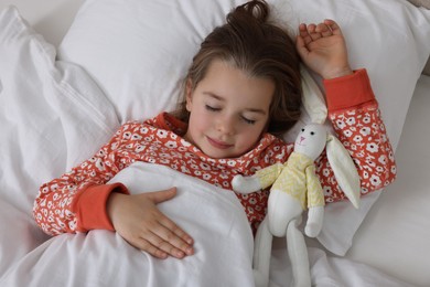 Photo of Cute little girl with toy bunny sleeping in bed, top view