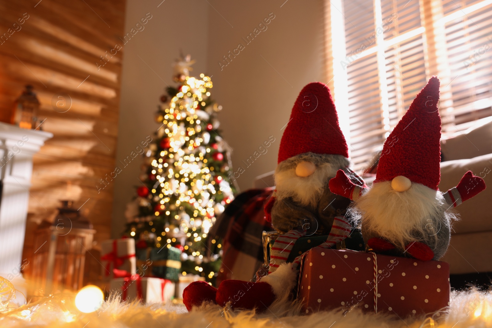 Photo of Cute Christmas gnomes and gift in room with festive decorations. Space for text