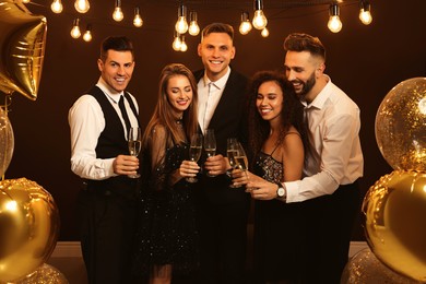 Happy friends with glasses of sparkling wine celebrating New Year indoors