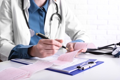 Doctor examining cardiogram at table in clinic, closeup