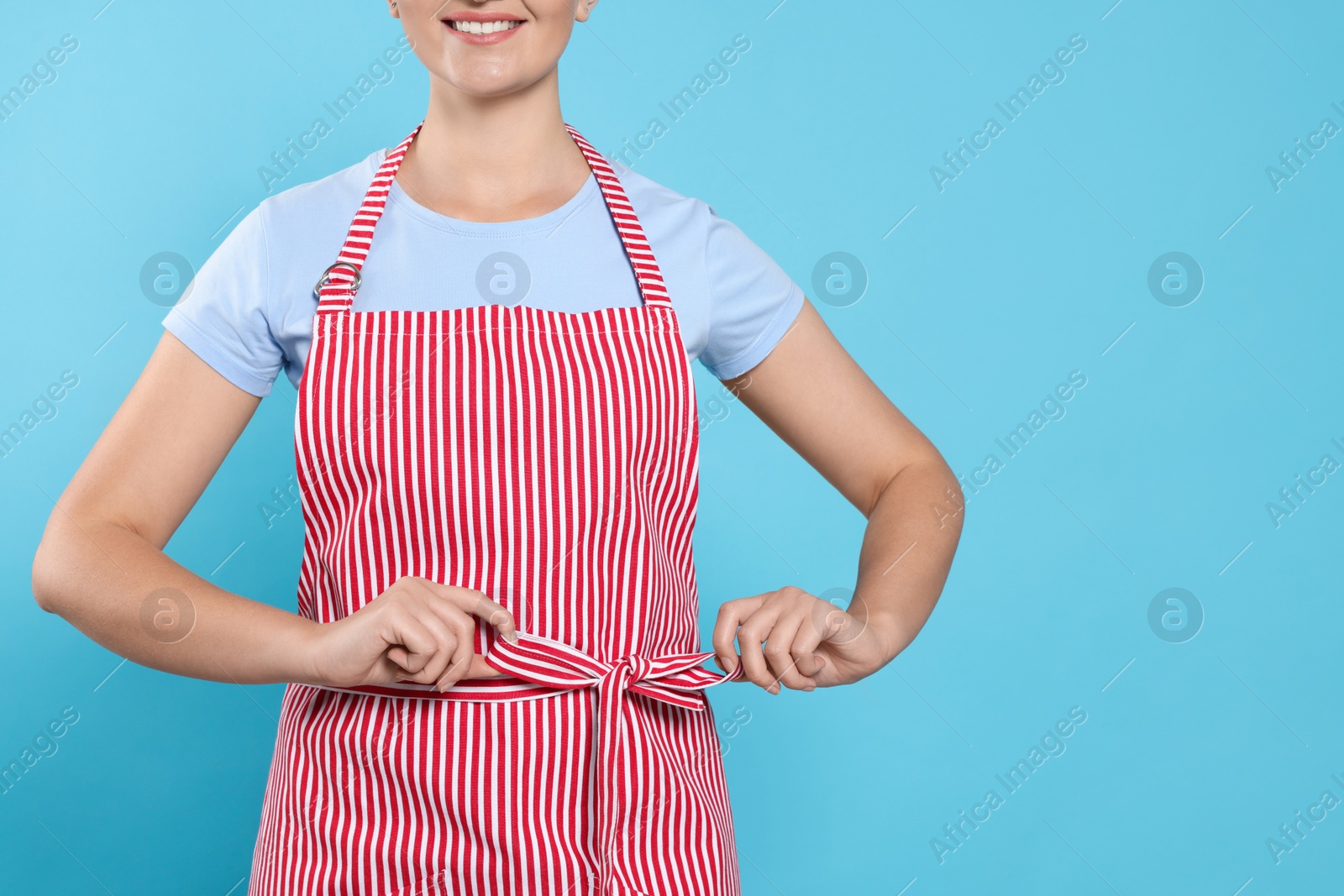 Photo of Woman in clean striped apron on light blue background, closeup