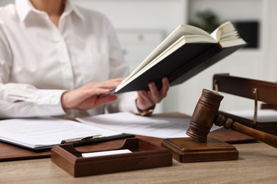 Photo of Lawyer working with documents at wooden table in office, focus on gavel