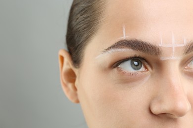 Eyebrow correction. Young woman with markings on face against grey background, closeup. Space for text