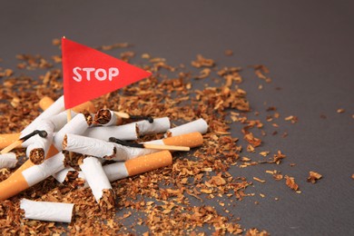 Photo of Red flag with word Stop, broken cigarettes and burnt matches on dark grey background, closeup with space for text. Quitting smoking concept
