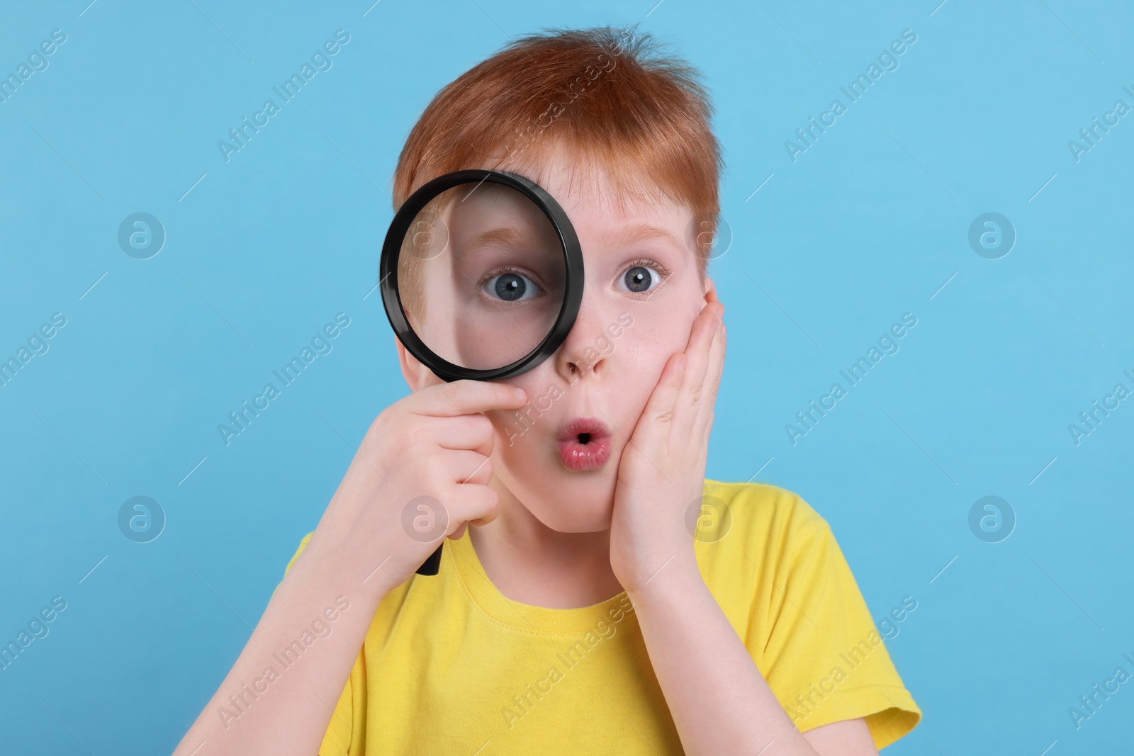 Photo of Surprised boy looking through magnifier glass on light blue background