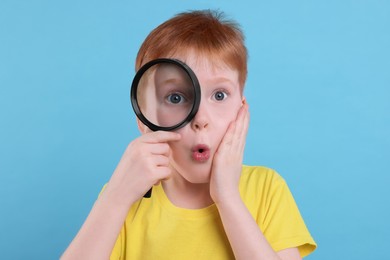 Photo of Surprised boy looking through magnifier glass on light blue background
