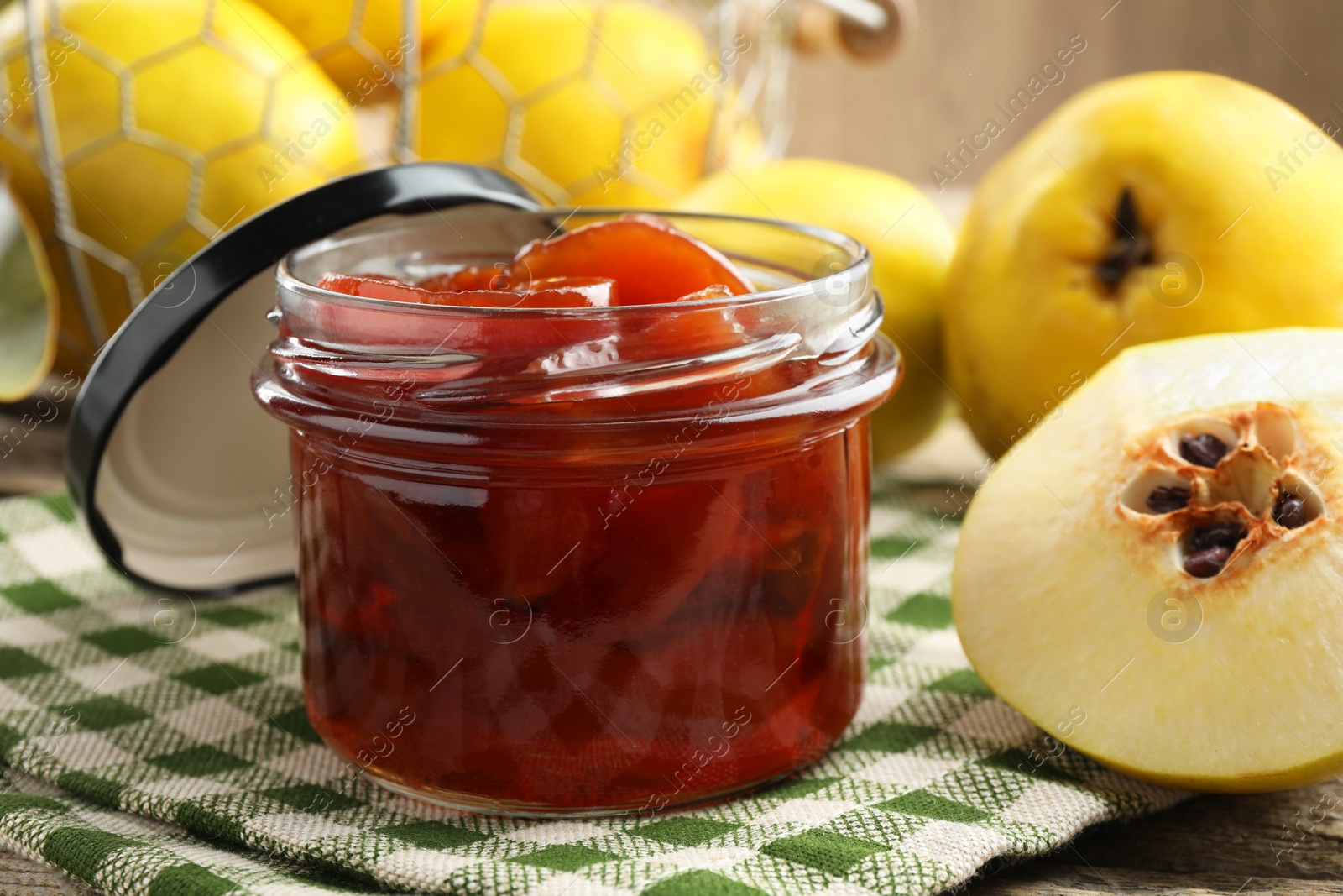 Photo of Tasty homemade quince jam in jar and fruits on wooden table, closeup