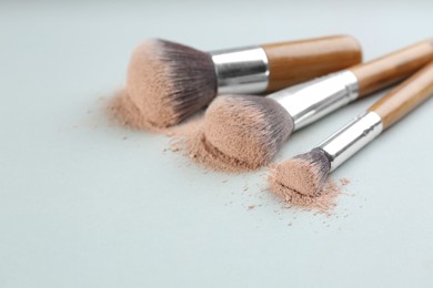 Photo of Different makeup brushes with crushed cosmetic product on light background, closeup. Space for text