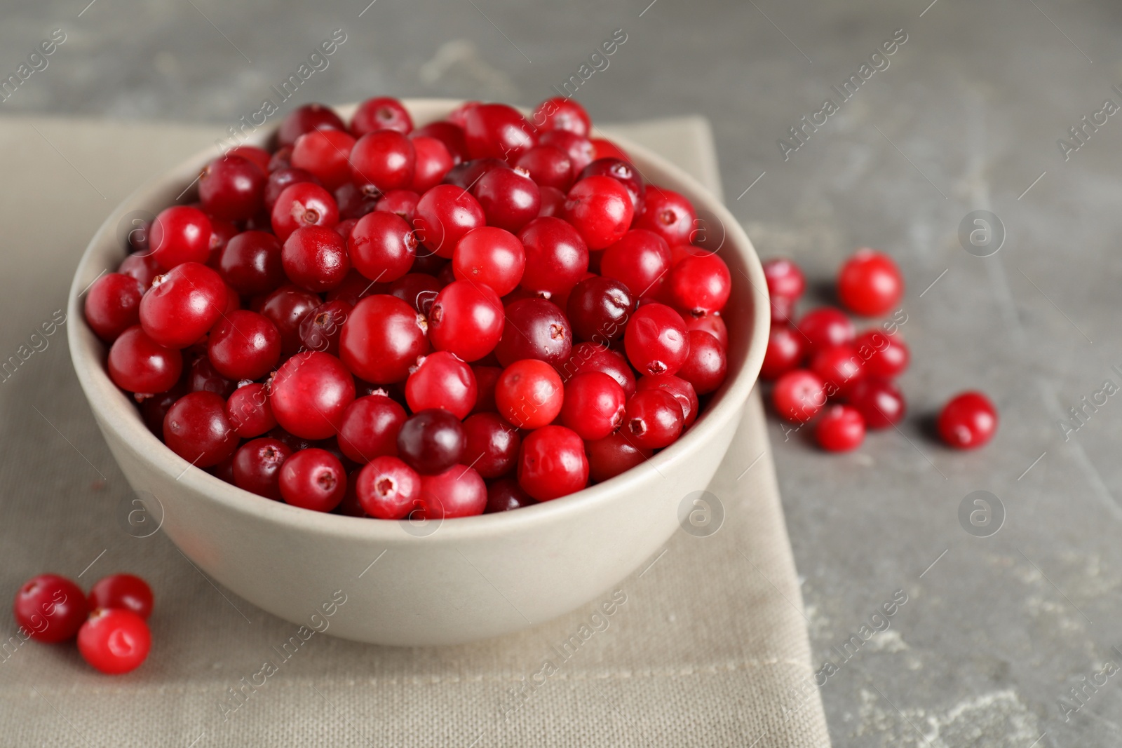 Photo of Cranberries in bowl on light grey table, closeup